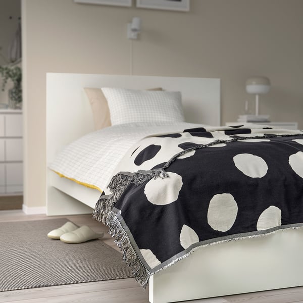 Bedroom with KLYNNETÅG polka dot throw on white bed, slippers nearby.