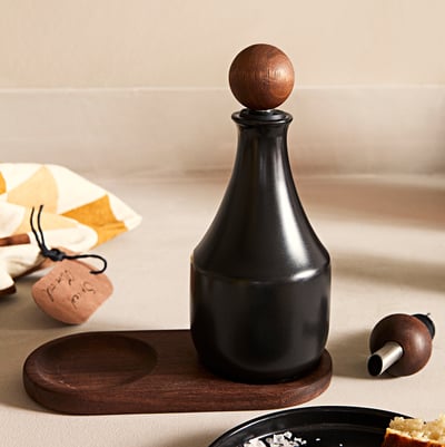 KRÖSAMOS black ceramic bottle with wooden top and drip stopper on wood tray.