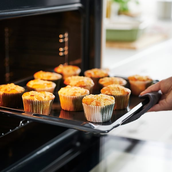 Hand holding tray of golden muffins in colourful liners being removed from oven.