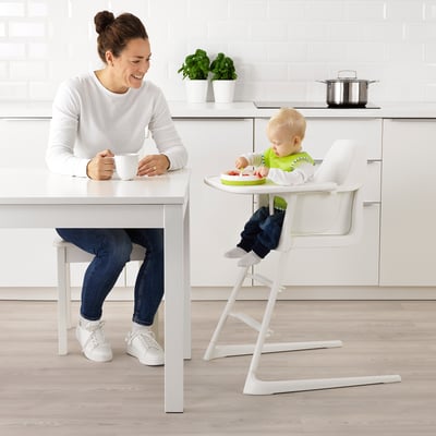Person drinks coffee in kitchen while baby eats.
