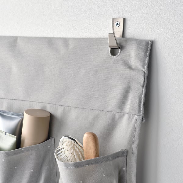 Grey hanging organiser with pockets holding items, attached to wall hook. Ideal for storing bathroom essentials or baby items.