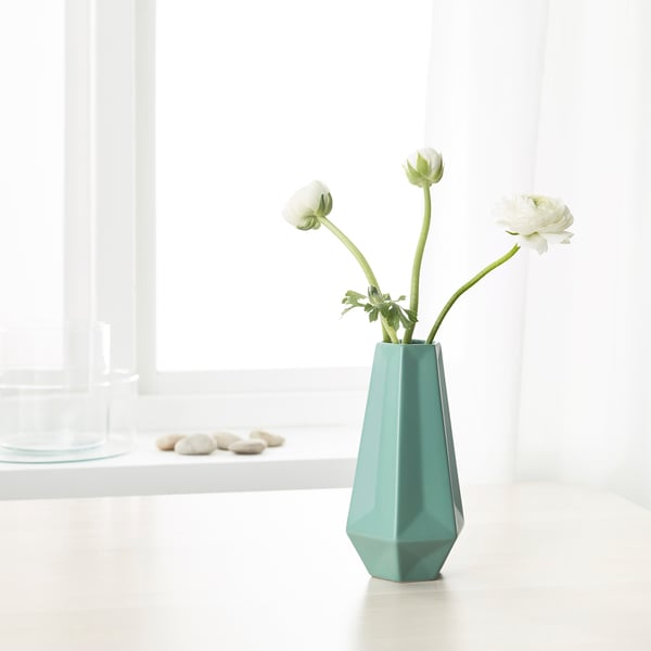 Geometric teal vase holding white flowers on a table. Bright, minimalist decor.