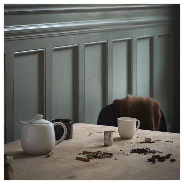 Cosy tea setup on wooden table with blue wall. Kettle, strainer, mug, tea, and cinnamon.