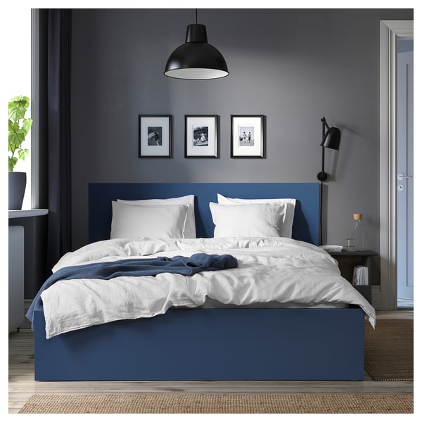 Blue MALM bed, white linens, framed photos, lamps, door open, throw blanket, plant, rug.