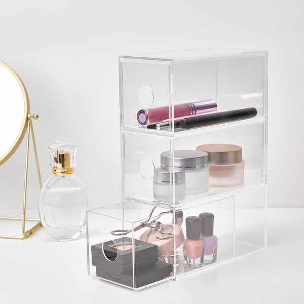 Clear acrylic makeup organiser with 3 drawers, storing lipsticks, jars, and nail polishes, shown upright on a white surface.