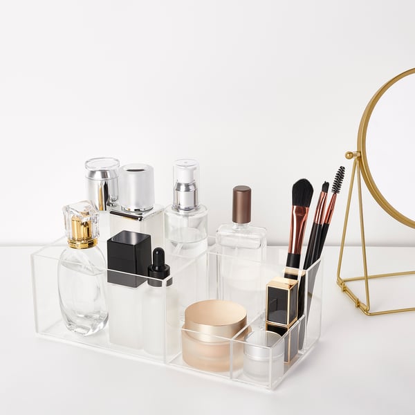 Clear acrylic storage organiser with multiple compartments, holding cosmetics, brushes, and accessories neatly.