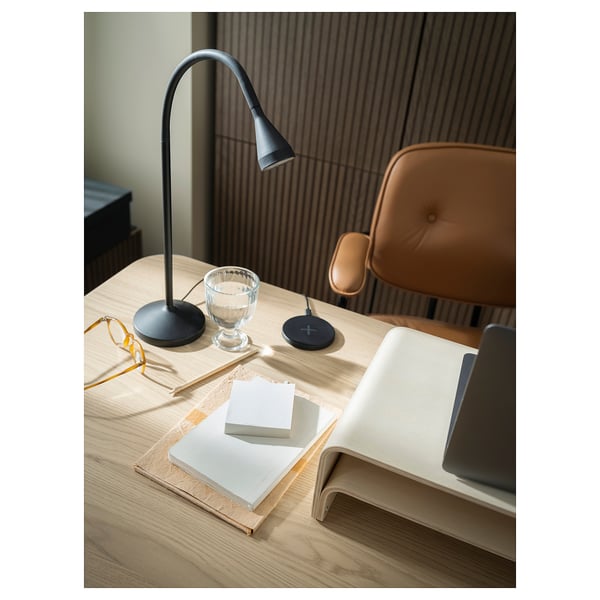 Well-lit home office with NÄVLINGE black modern lamp on wooden desk, brown chair, books, and tech devices.