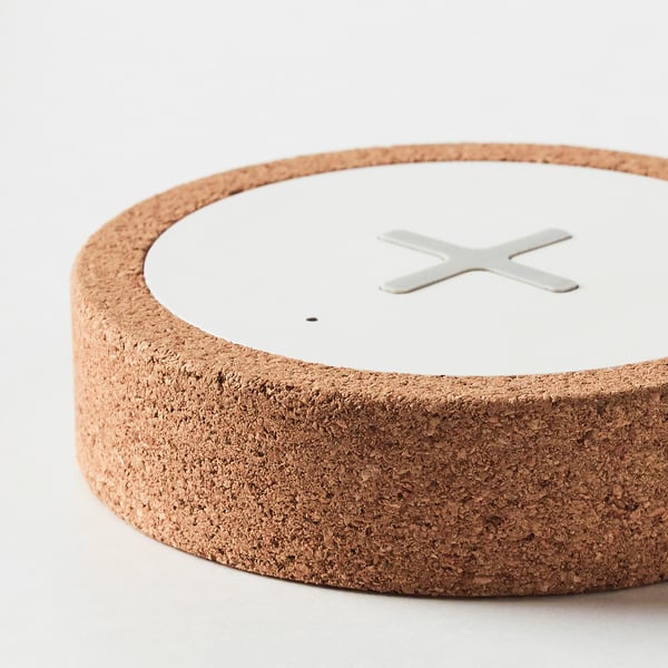 Round wireless charger with textured cork exterior, smooth white top, and metallic charging symbol.