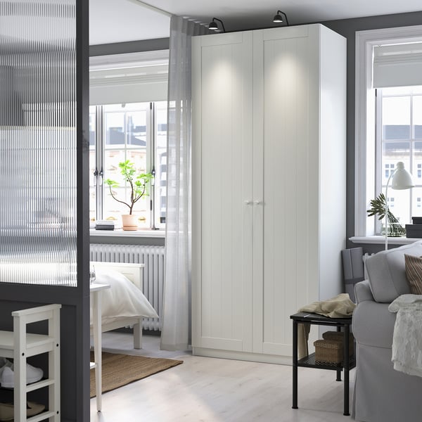 Spacious white PAX wardrobe fits neatly next to a grey sofa, dominating the room with its tall, rectangular shape and clean design.