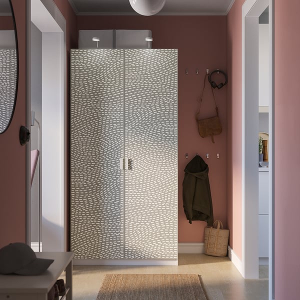 Modern bedroom with patterned PAX wardrobe, pink walls, woven rug, and personal items.