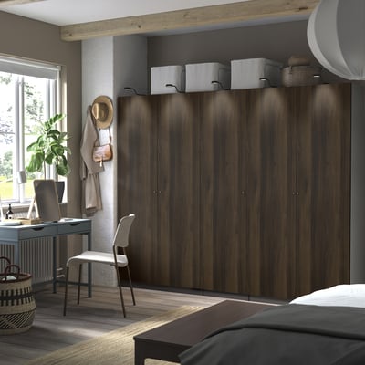 Modern bedroom with PAX wardrobe, chair, desk, plant, and wooden ceiling beam.