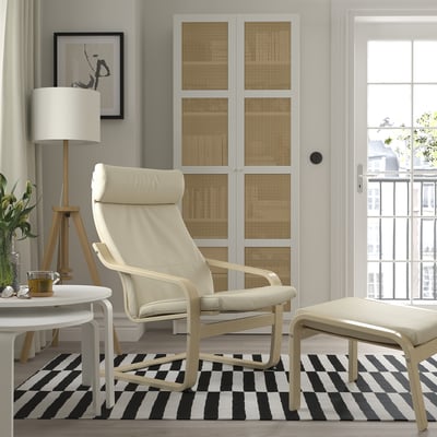 Stylish living room with POÄNG armchair, footstool, side table, lamp, striped rug, canvas print, and large window.