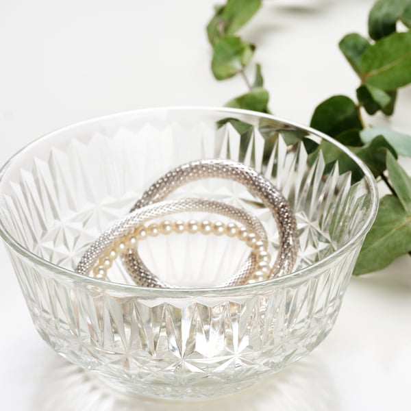 Clear glass bowl with cut-glass pattern holds jewellery, elegant for display or storage.