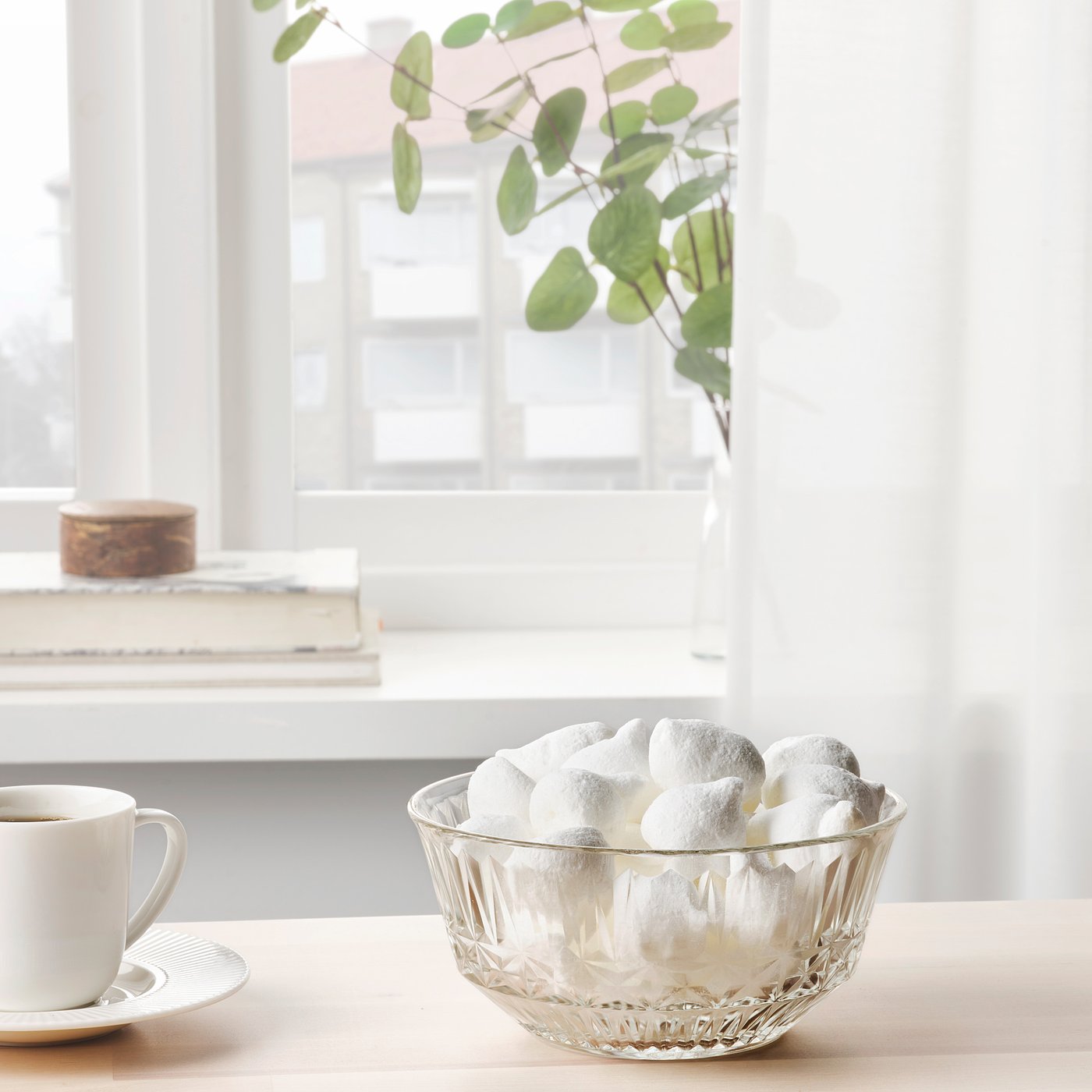 Bowl of powdered donut holes on a table by a window with a cup of coffee.