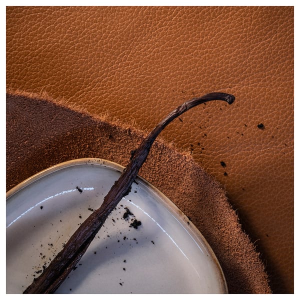Warm candle with wooden wick resting on leather surface. Silent, cosy atmosphere.