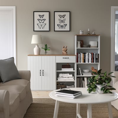 Living room with SKRUVBY sideboard & bookcase, decorated with plants, books, and butterfly art, and a cosy sofa.