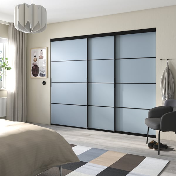 Modern bedroom with blue-gray sliding closet doors, light wooden floor, bed with beige blanket, striped rug, and hanging light fixture.