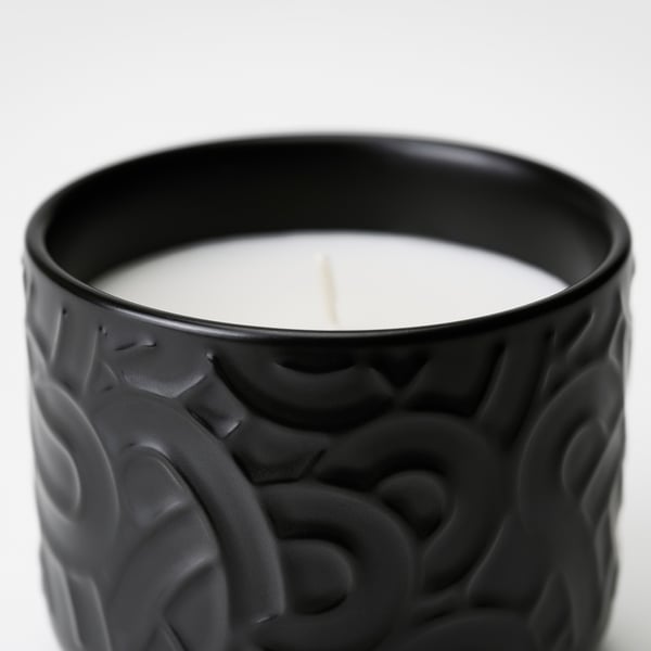 Black stoneware candle with intricate designs. ’illed wick emits a subtle glow.