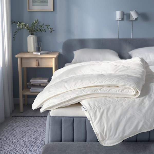 White STJÄRNBRÄCKA duvet on grey bed, blue walls. Neatly folded, soft. Bedside table with plants, water, books.