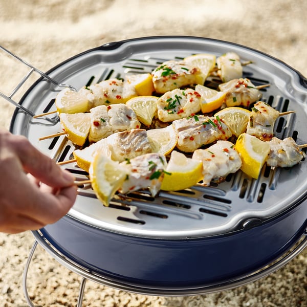 Lemony fish skewers grilling on STRANDÖNs portable, well-vented charcoal grill with tongs.