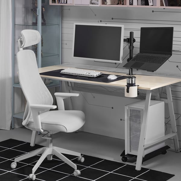 Minimalist home office: STUBBERGET laptop stand, desk chair, monitor, keyboard, placemat, and cup on grey desk; bookshelf, window.