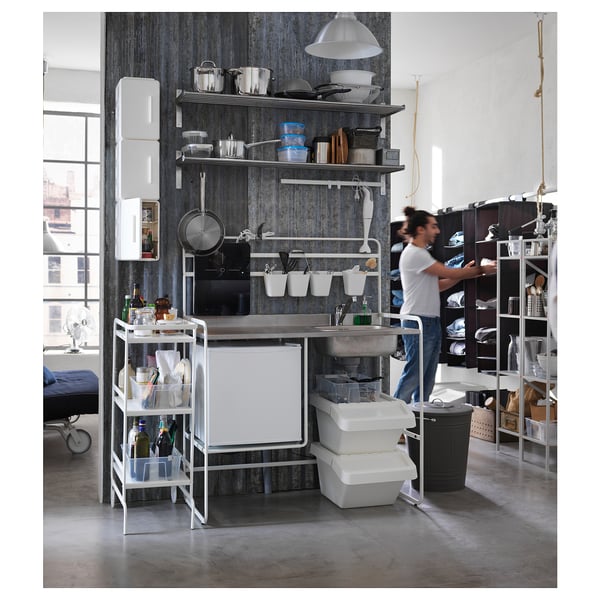 Modern compact kitchen with stainless steel sink, white cabinets, and open shelving. A person is organising items beside it.