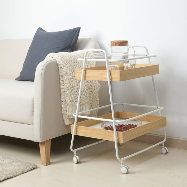 Beige SVENARUM trolley table next to white sofa, with blue decor and wheels.