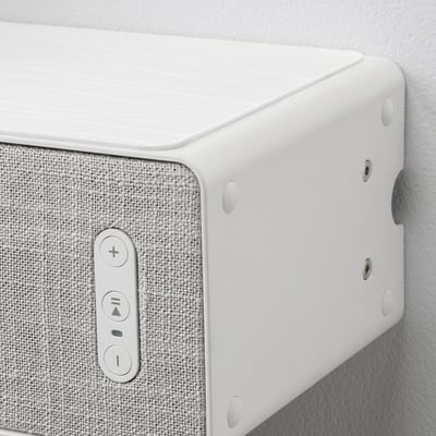 Close-up of white wall-mounted speaker with controls and screws.