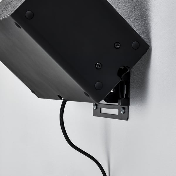 Black wall-mounted speaker bracket securely attached, cable visible.