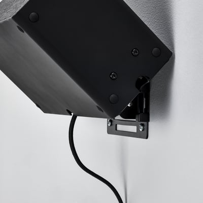 Black wall-mounted speaker bracket securely attached, cable visible.