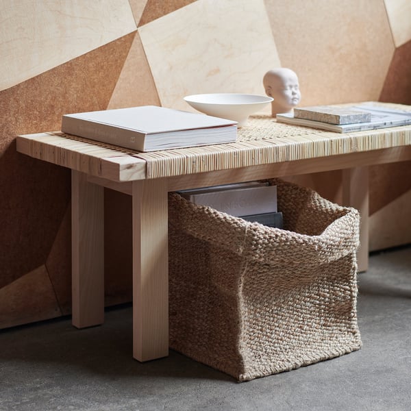 Natural jute TJILLEVIPS basket on wooden table, holding books and bowl. Soft, woven design.