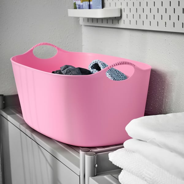 Bright pink TORKIS laundry basket on shelf, filled with clothes, made of flexible plastic.
