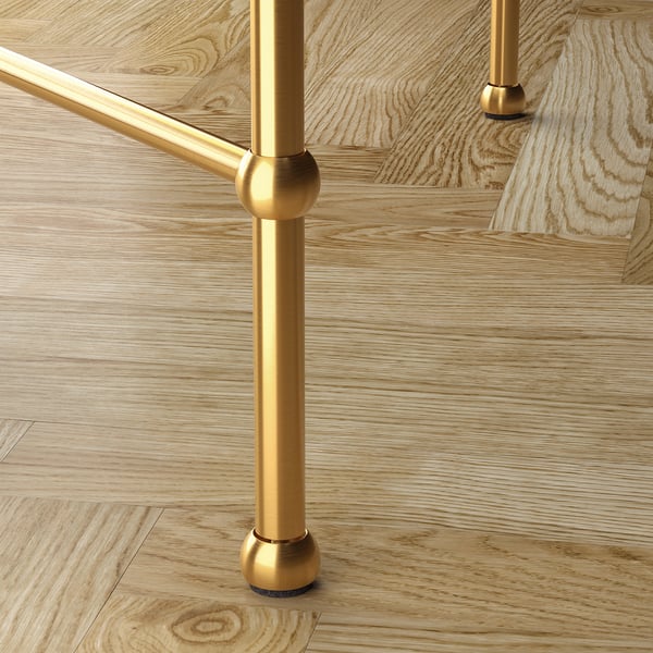 Golden metal legs of a glass-top table, showcasing elegant craftsmanship and stability with adjustable feet on a wooden floor.