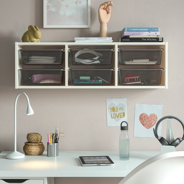 Compact white TROFAST wall unit, featuring mesh storage boxes, holding various items, situated above a white desk with accessories.