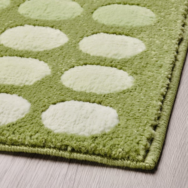 Green and white dotted door mat, soft texture, placed on a wooden floor.