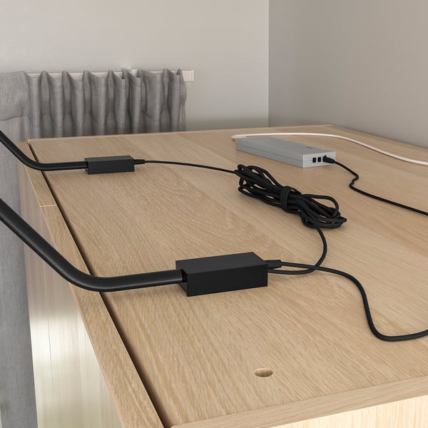 Wooden desk with two black corded devices and cables, one grey box with cables connected.