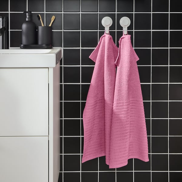 Pink VÅGSJÖN towels hang on hooks beside a dark tile wall with a white sink.