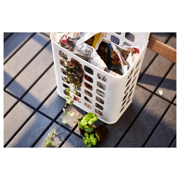 White VARIERA plastic bin filled with items, placed on a metal grate table, surrounded by small potted plants.
