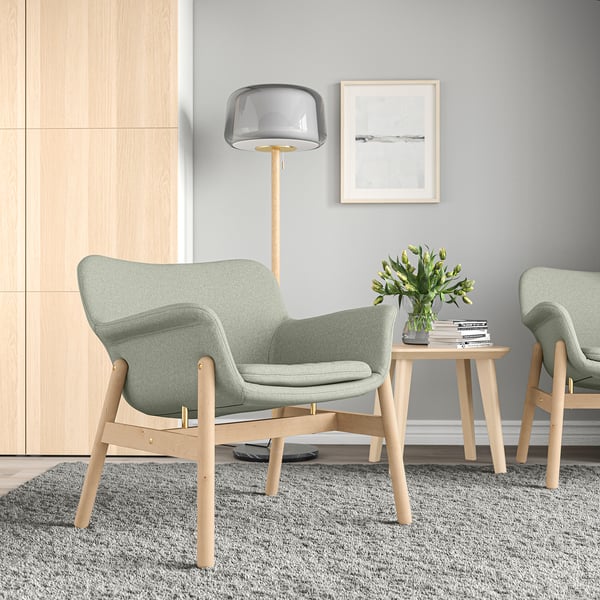 VEDBO armchairs, sage green, wood & fabric, curved, minimalist. Small, set on rug, beside table with flowers.