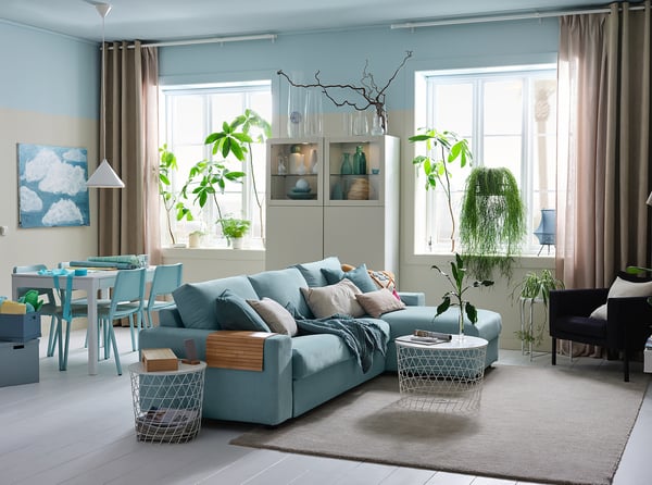 Modern living room with light blue VIMLE sofa, wooden coffee table, white rug, and large windows with beige curtains.