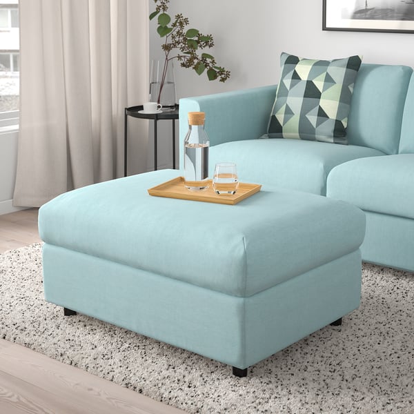Light blue VIMLE ottoman, worn under sofa. Rectangular, soft, large enough for drinks, legs, or extra seating.