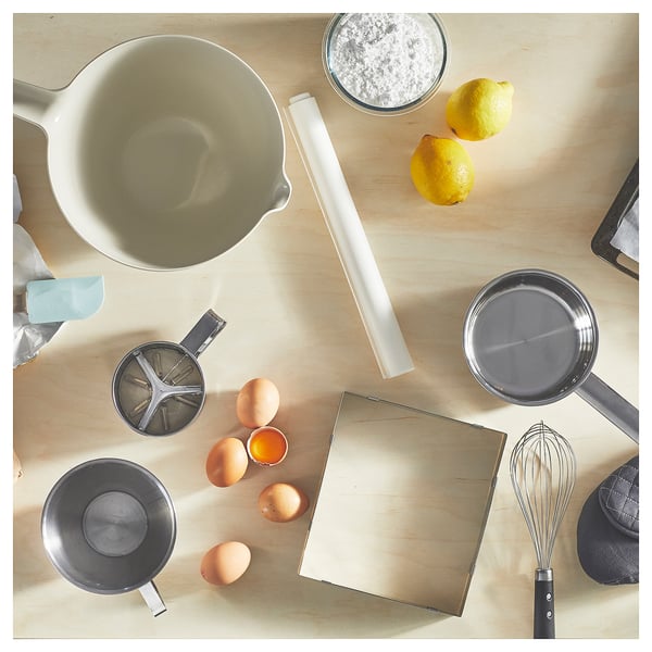 A white VISPNING mixing bowl and various baking ingredients and tools on a wooden surface.