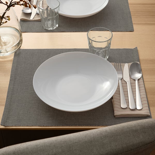 Elegant VITBLECKA setting: white, round bowl on grey mat, metal utensils, clear cups; table decor.