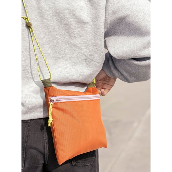 Small orange crossbody bag, ÅBORDSÖN, worn over grey sweater, made of 100% polyester.
