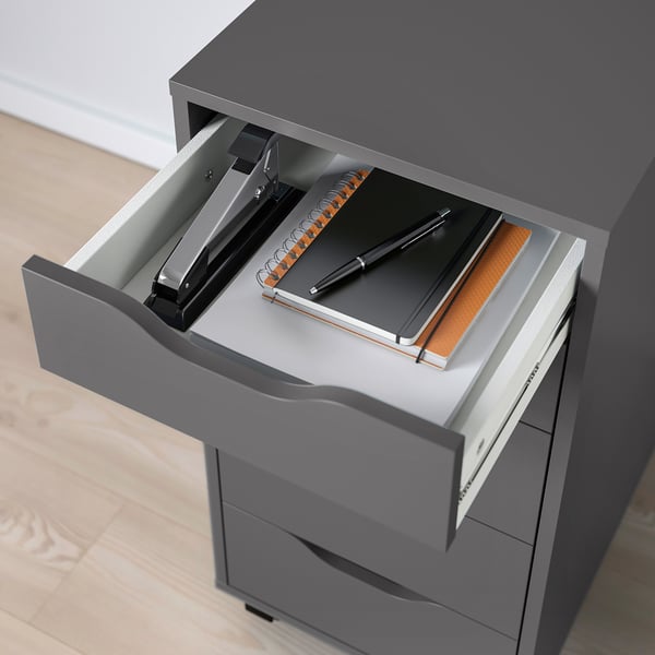 Open grey filing cabinet drawer with stapler, notebook, and pen.