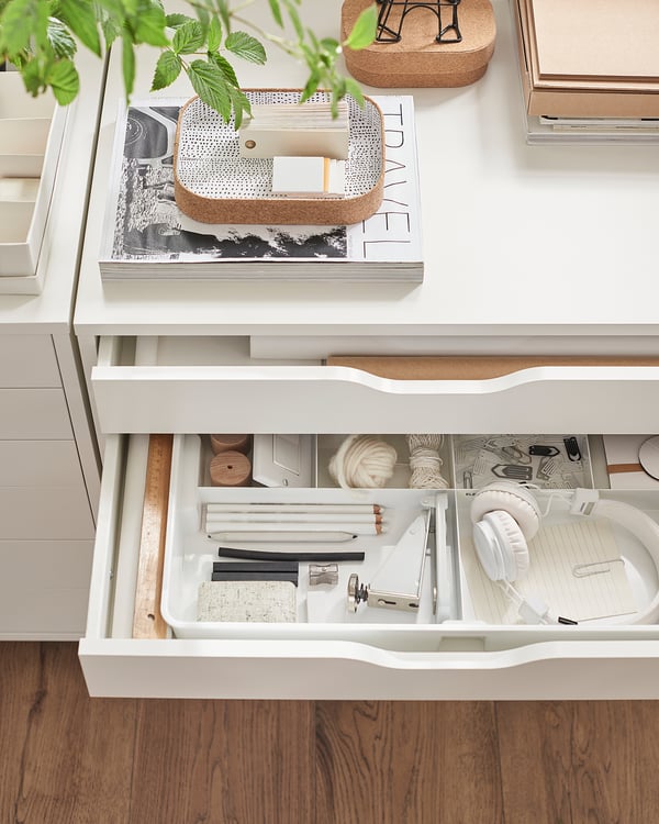 White ALEX drawers, organised with office supplies, books, and plants. Top drawer open, showing compartments.