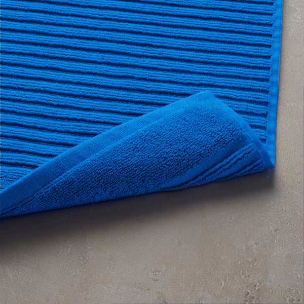 Bright blue bath mat with wavy pattern on textured concrete, displayed folded.