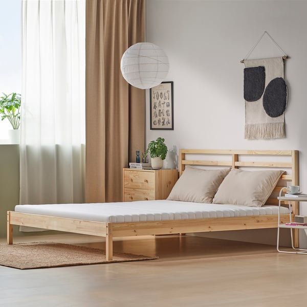 Cosy bedroom with wooden bed, beige mattress, light pillows, wooden furniture, decor, rug, and large window.