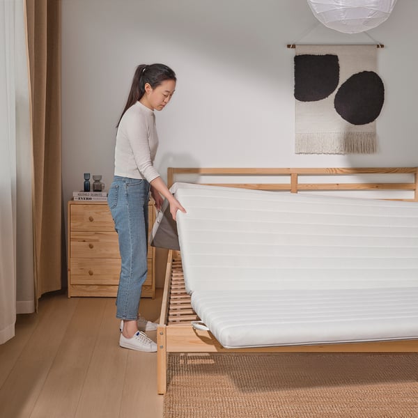 Person sets up coir and foam mattress on wooden bed frame.