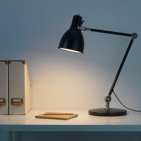 Black adjustable work lamp on desk, illuminating stack of books, with white light.
